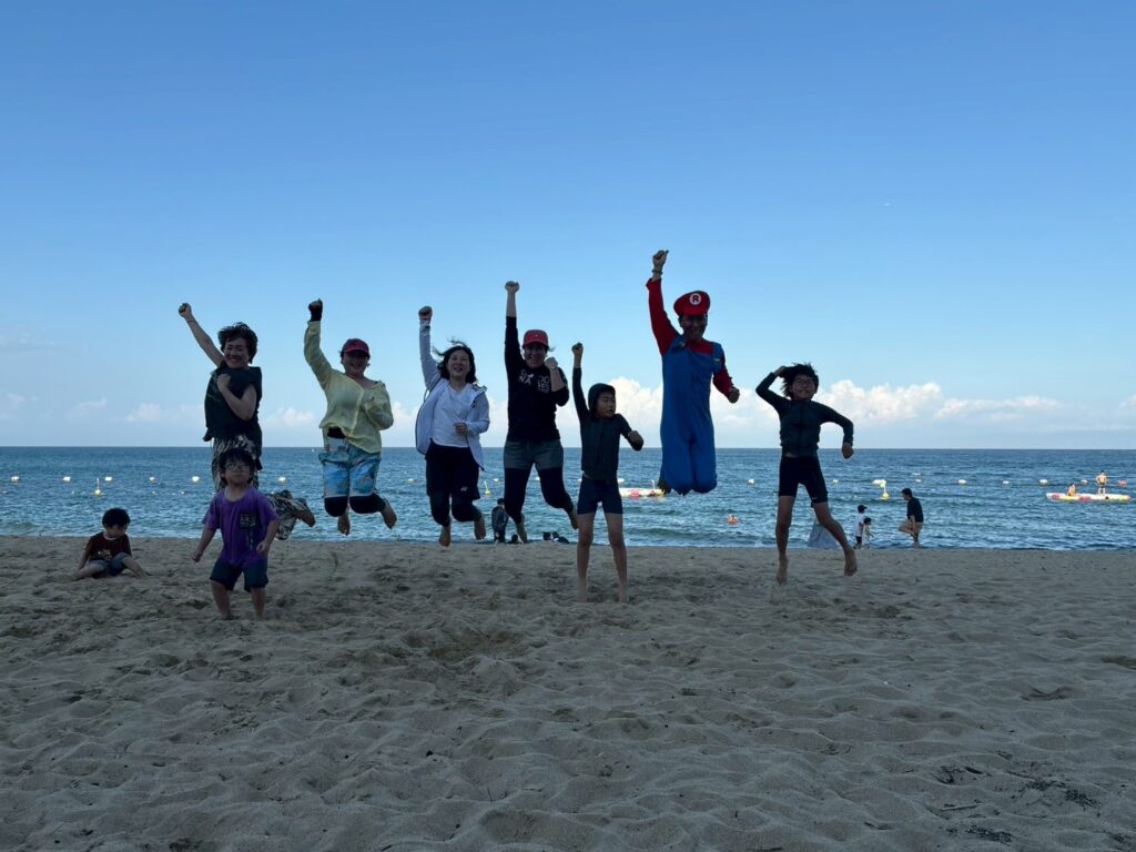 浜辺で仲間たちとジャンプする写真｜德永晴香